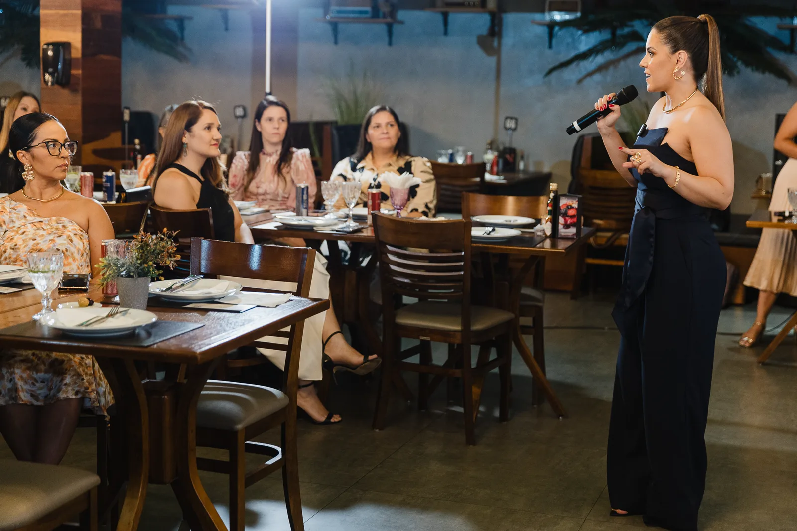 Mari Davantel conduzindo uma aula presencial com microfone, diante de mulheres sentadas às mesas